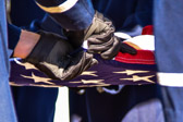 The Flag is carefully folded into the shape of a tri-cornered hat, emblematic of the hats worn by colonial soldiers during the war for Independence.