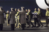 Marine carry team carries transfer case of Cpl. Kevin J. Reinhard  to the mortuary transfer vehicle.  Dignified transfer officer orders “Present, Arms” (slow movement salute)