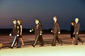 Carry team follows (by walking) transfer vehicle, with the transfer vehicle guide walking behind the carry team.  Dignified transfer officer and senior ranking officer follow (walking) behind the transfer vehicle guide, ending the dignified transfer